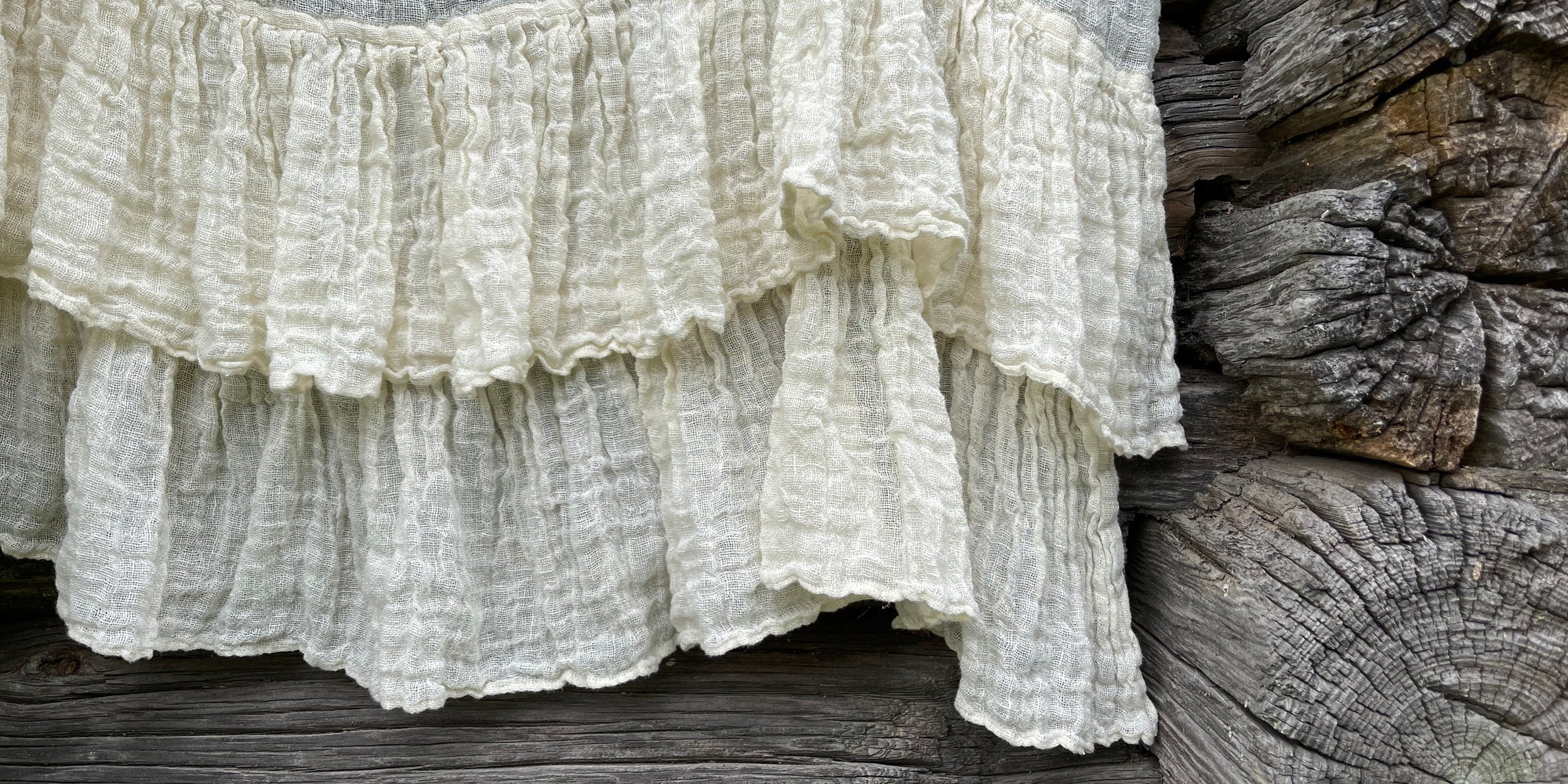 Gauzy ruffled linen curtain in an ivory white on a old grey log background